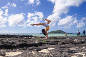 Grace Koh performs an elaborate handstand on a rocky beach.