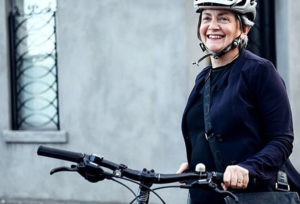 A woman wearing a helmet is stands next to a bike.