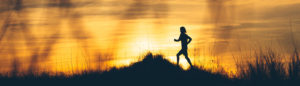 Silhouette of a person running through a grassy and hilly field.