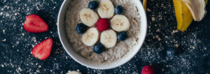 A bowl of porridge decorated with chopped banana, blueberries , raspberries and strawberries.