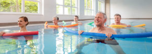 A mixed group of adults using pool noodles for exercise during an aquatic therapy class in the pool.