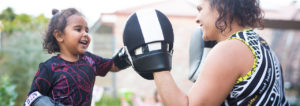 Four year old Yindi smiling as she practices boxing with her mother, Nikita, outside.