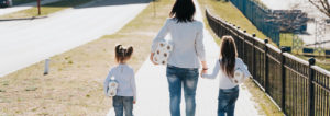 Woman walking with two young girls, all are carrying toilet paper rolls.