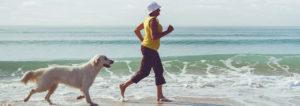 Woman running along beach with her dog.