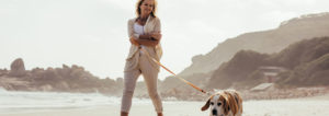 Woman walking dog along beach.